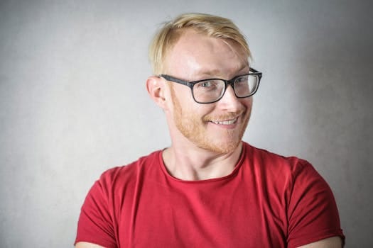 Portrait of a young blonde man in red shirt smiling with eyeglasses.