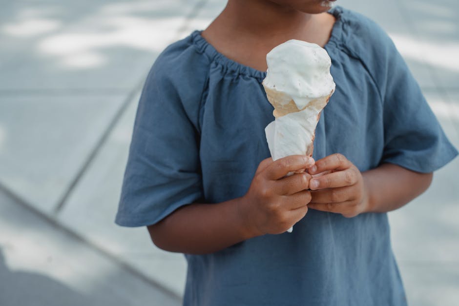 Crop anonymous girl in casual outfit with tasty sweet melting ice cream cone in hands