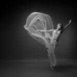Graceful ballet dancer with flowing fabric in a dramatic black and white photo.