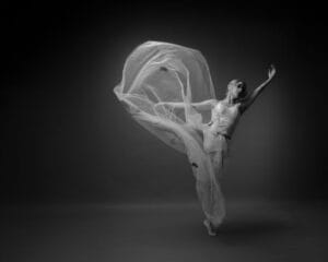 Graceful ballet dancer with flowing fabric in a dramatic black and white photo.