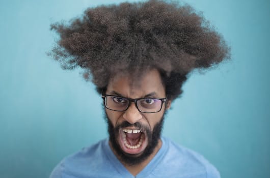 Portrait of a man with afro hair wearing eyeglasses, expressing emotion against a blue background.
