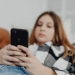 Teenage girl using smartphone while relaxing on a sofa, depicting leisure and connectivity.