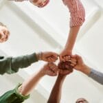 Four diverse team members join fists together, displaying unity and teamwork.