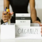 Close-up of hands organizing pens and notes in a white box labeled 'Organize.' Perfect for productivity inspiration.