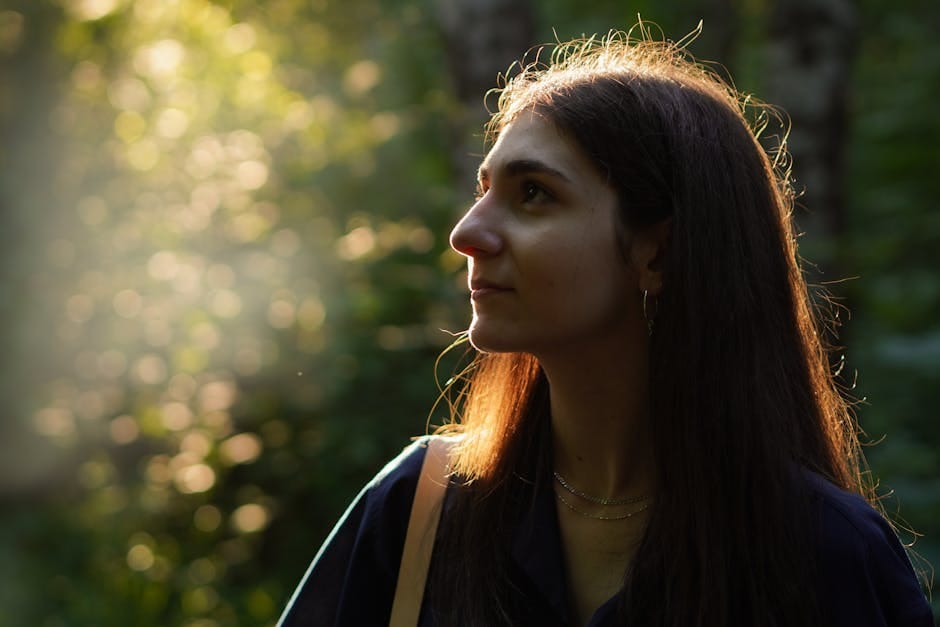 Profile of a woman in a sunlit forest, exuding tranquility and natural beauty.