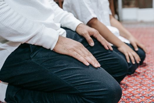 A close-up of individuals kneeling in prayer on a red patterned carpet indoors.